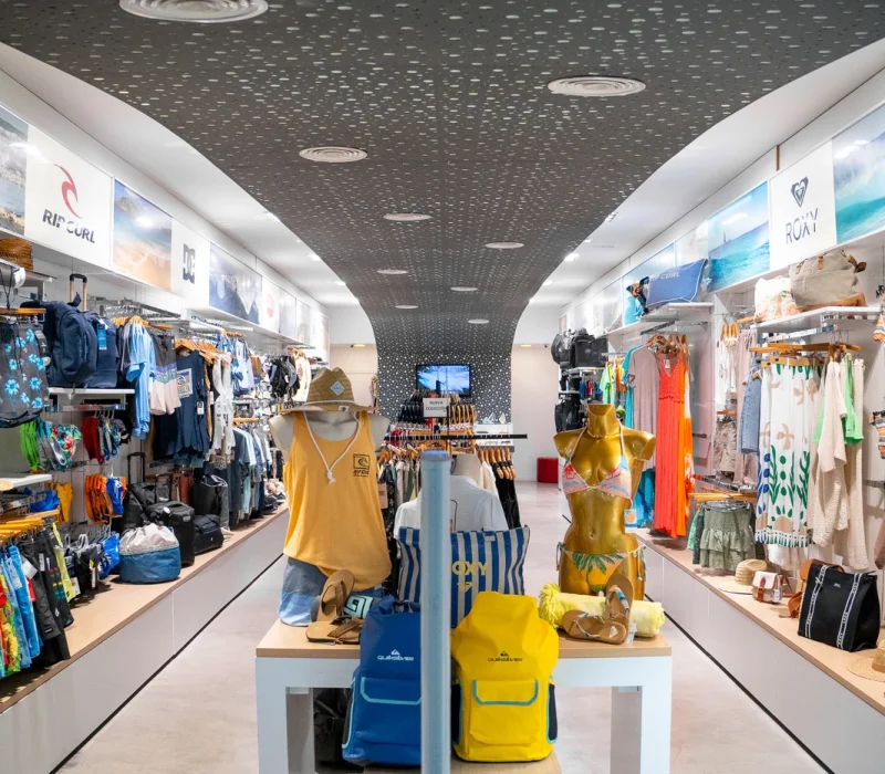 Tienda de ropa de surf con nueva colección en Lanzarote, mostrando camisetas, mochilas y accesorios de moda surf.