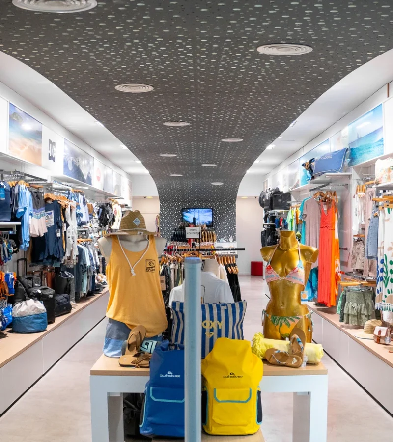 Tienda de ropa de surf con nueva colección en Lanzarote, mostrando camisetas, mochilas y accesorios de moda surf.