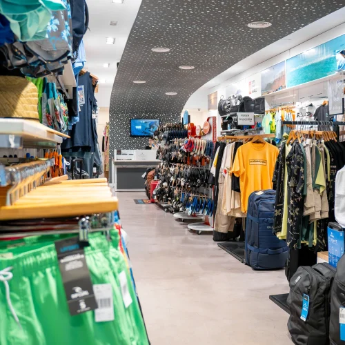 Tienda de ropa de surf con nueva colección en Lanzarote, mostrando camisetas, mochilas y accesorios de moda surf.