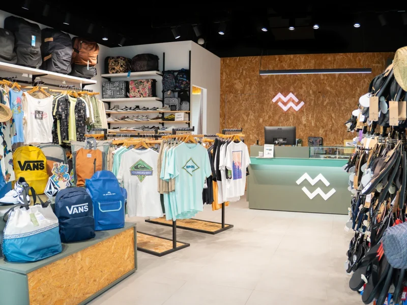 Tienda de ropa de surf con nueva colección en Lanzarote, mostrando camisetas, mochilas y accesorios de moda surf.