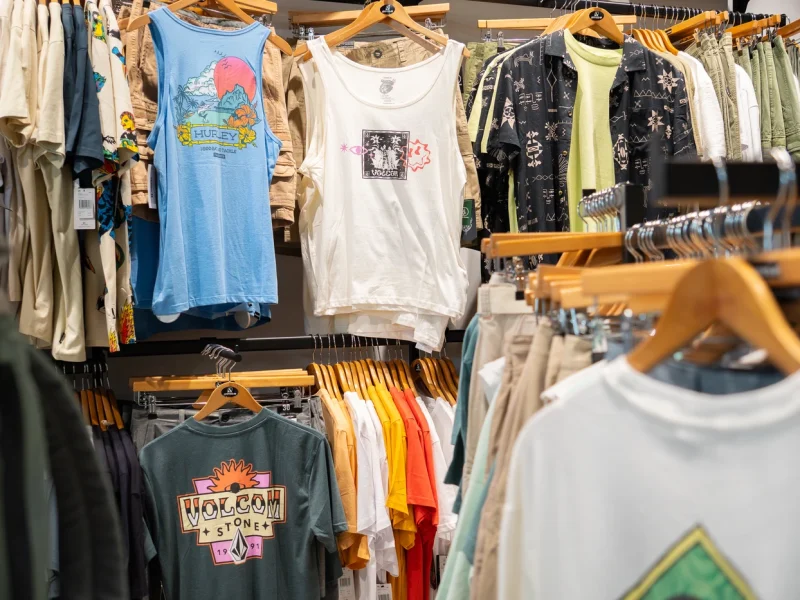 Tienda de ropa de surf con nueva colección en Lanzarote, mostrando camisetas, mochilas y accesorios de moda surf.
