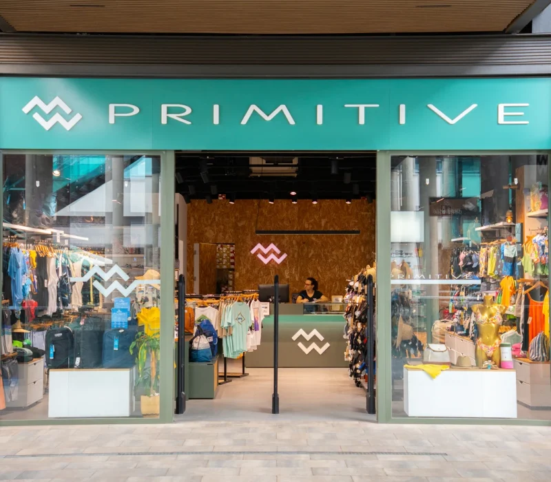 Tienda de ropa de surf con nueva colección en Lanzarote, mostrando camisetas, mochilas y accesorios de moda surf.