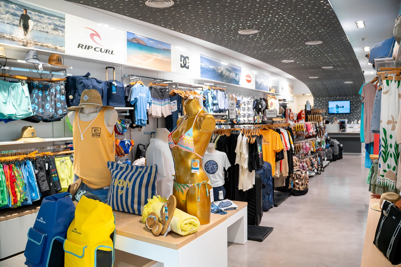 Tienda de ropa de surf con nueva colección en Lanzarote, mostrando camisetas, mochilas y accesorios de moda surf.