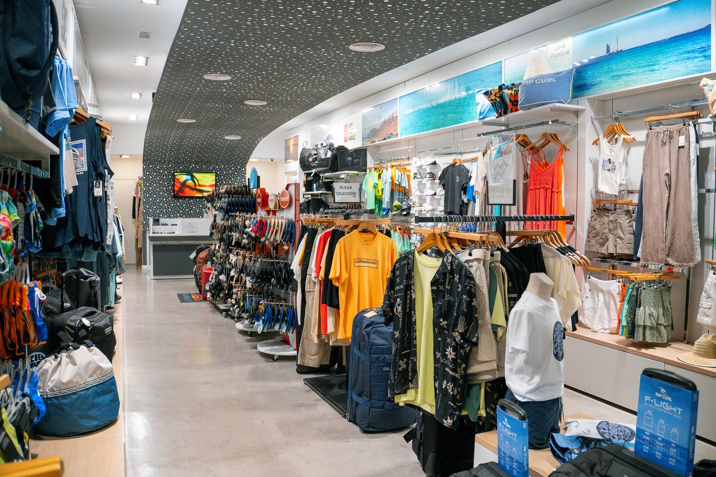 Tienda de ropa de surf con nueva colección en Lanzarote, mostrando camisetas, mochilas y accesorios de moda surf.