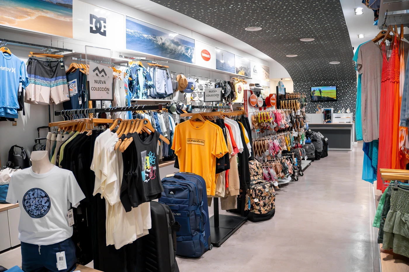 Tienda de ropa de surf con nueva colección en Lanzarote, mostrando camisetas, mochilas y accesorios de moda surf.