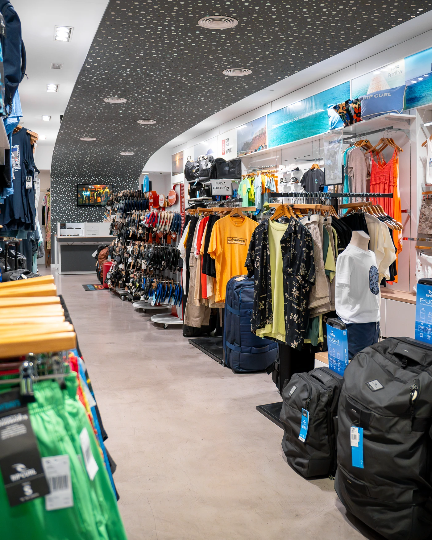 Tienda de ropa de surf con nueva colección en Lanzarote, mostrando camisetas, mochilas y accesorios de moda surf.