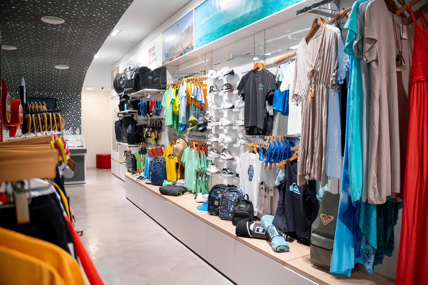 Tienda de ropa de surf con nueva colección en Lanzarote, mostrando camisetas, mochilas y accesorios de moda surf.